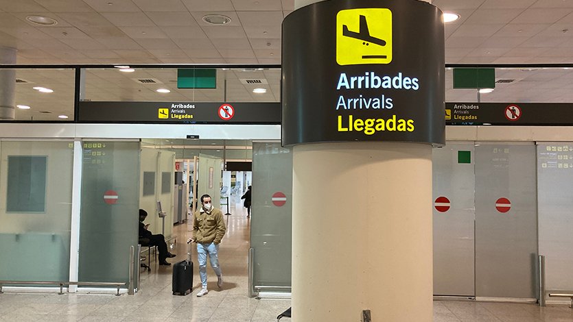 Pla general d'un senyal de la zona d'Arribades amb un passatger arrossegant una maleta de fons a l'Aeroport del Prat. Imatge del 23 de novembre de 2020.